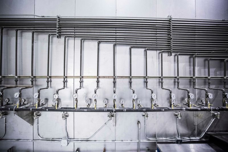 Red de cañerías industriales de acero con manómetros y válvulas alineados sobre una pared técnica