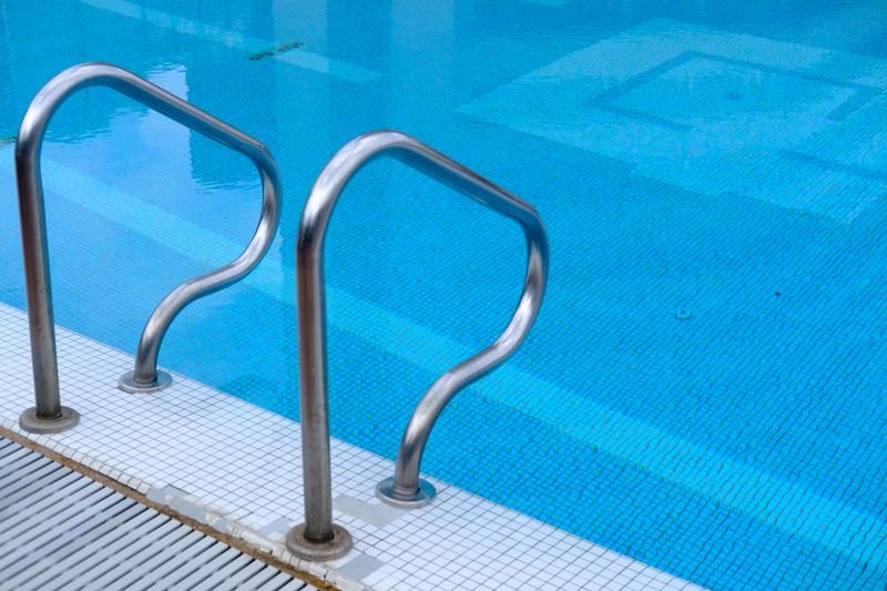 Borde de una piscina de agua celeste con escalera de acero inoxidable y revestimiento de mosaicos
